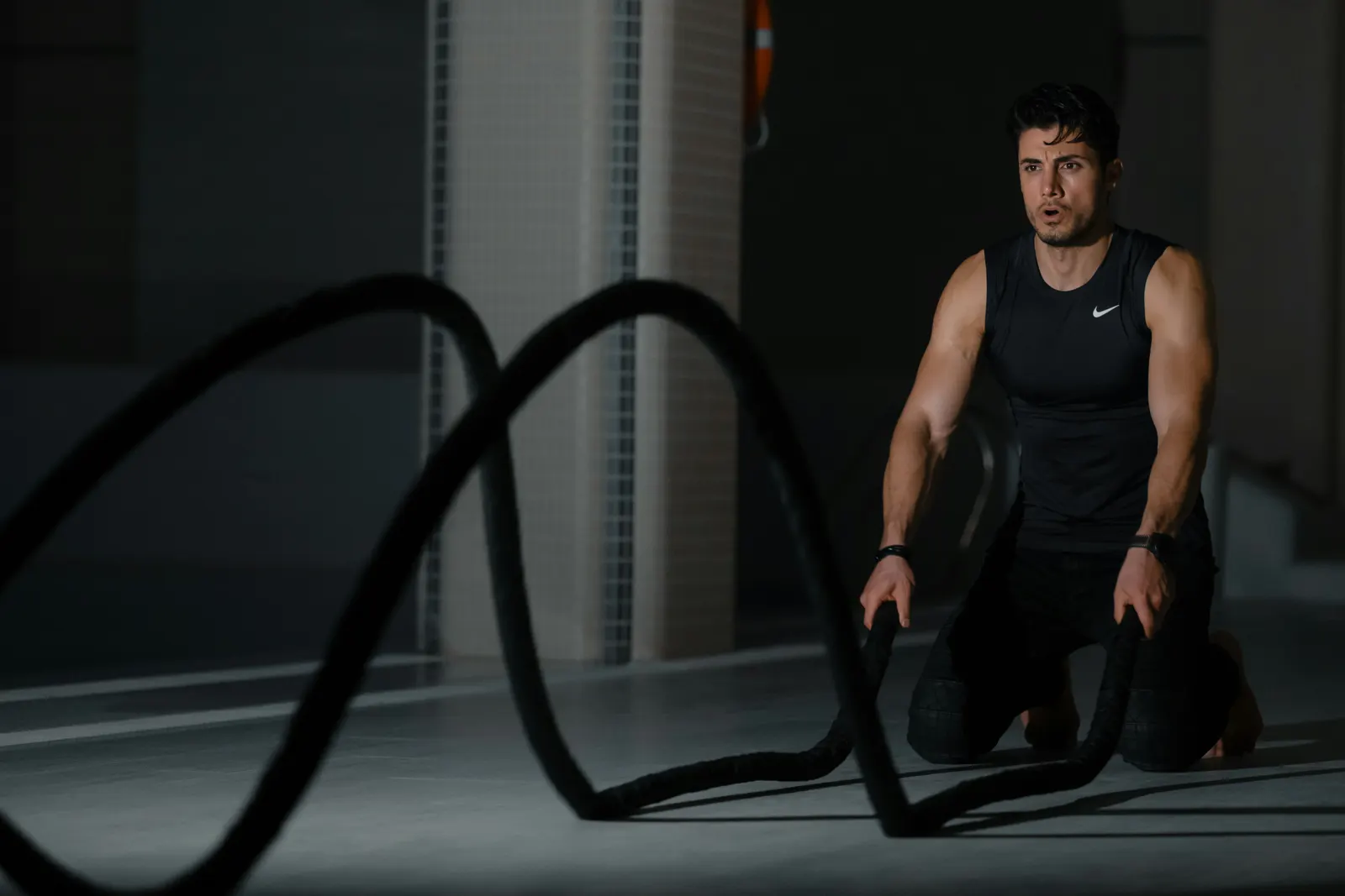 An athlete training with battle ropes in a dark, focused studio