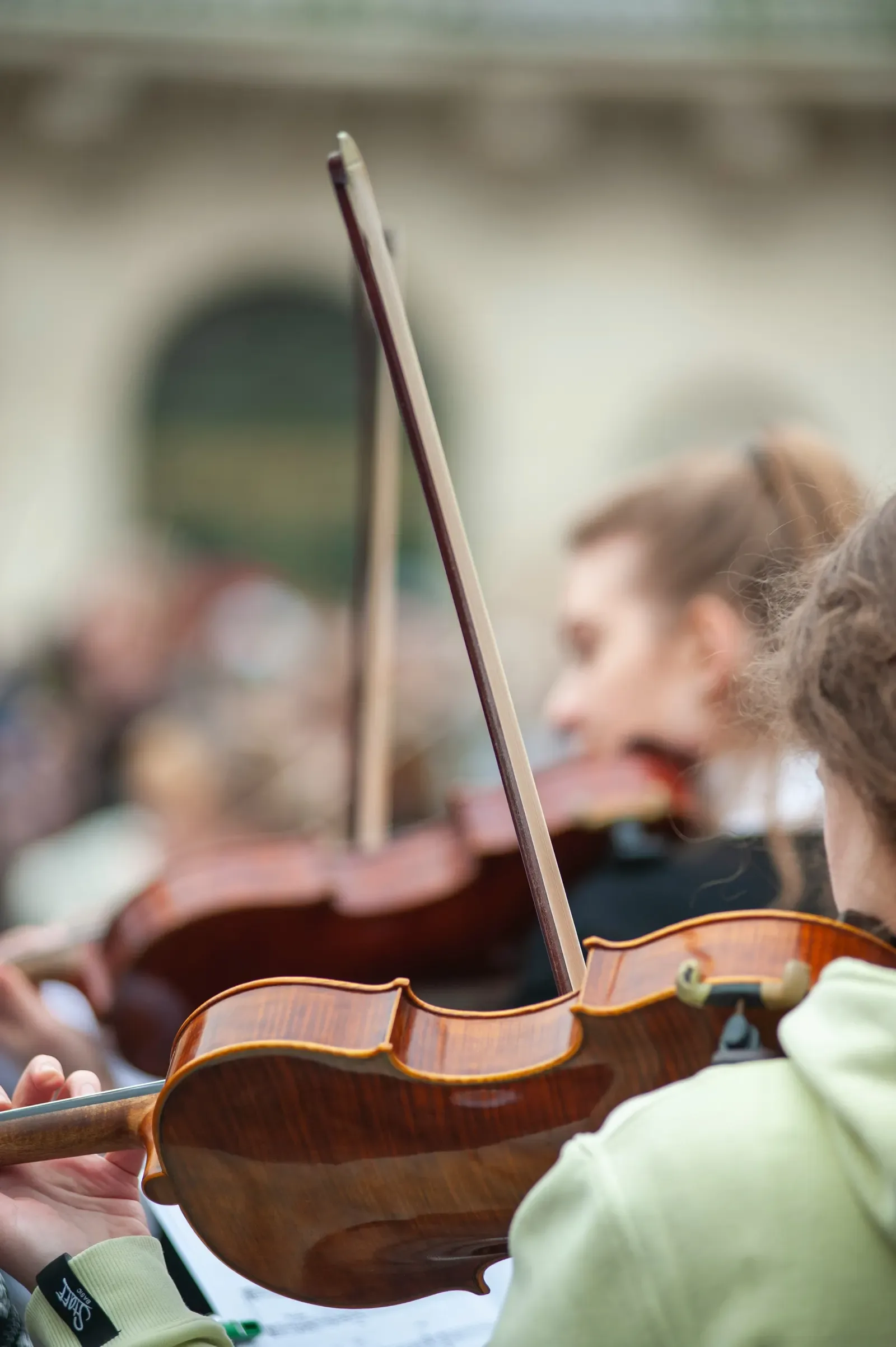 A student playing violin in a group lesson, bow raised mid-phrase